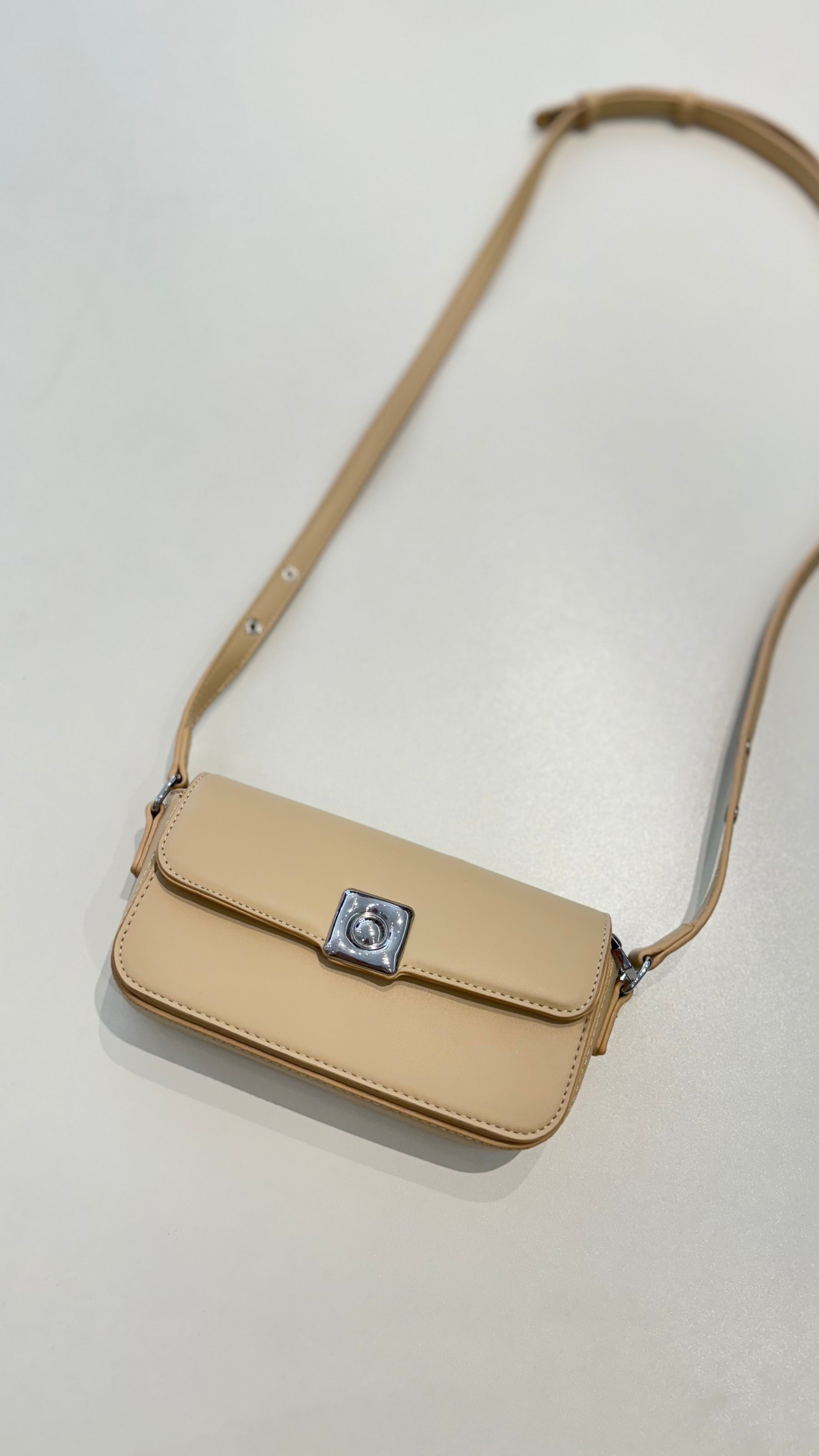 Bolsa Lia em couro legítimo bege, compacta e elegante. Design estruturado, alça regulável e detalhes em prata para usar no ombro ou transversal.