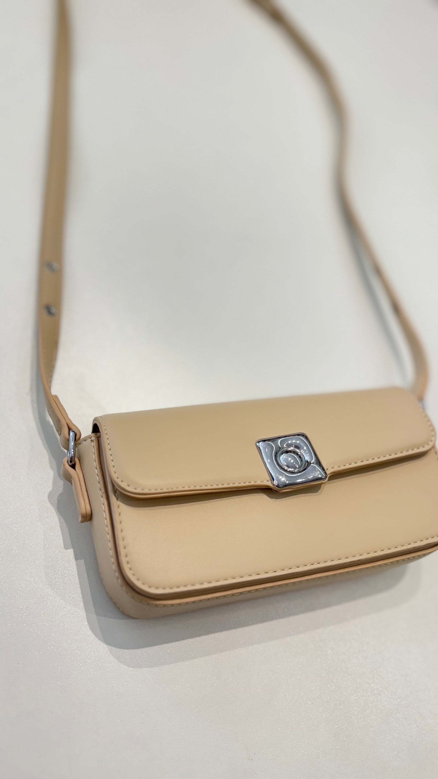 Bolsa Lia em couro legítimo bege, compacta e elegante. Design estruturado, alça regulável e detalhes em prata para usar no ombro ou transversal.