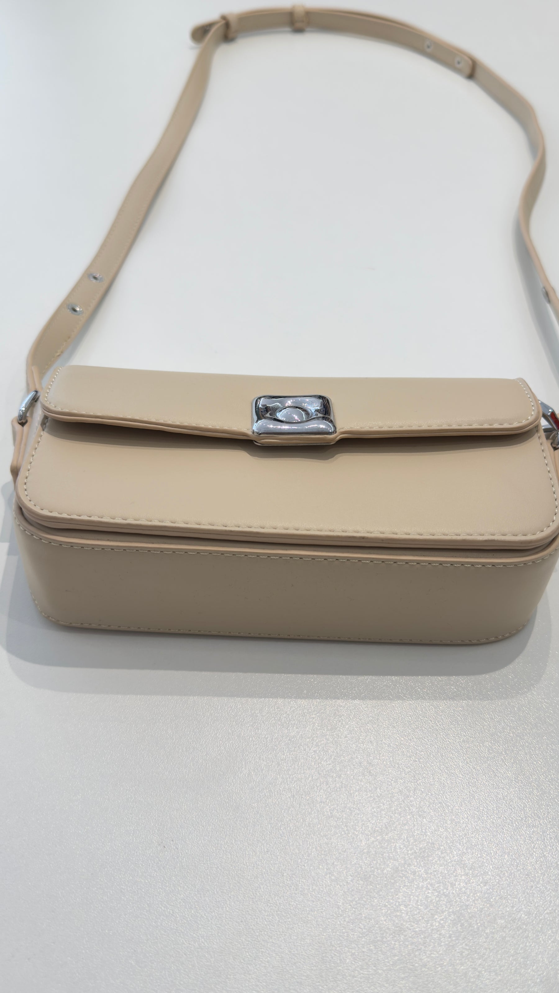 Bolsa Lia em couro legítimo bege, compacta e elegante. Design estruturado, alça regulável e detalhes em prata para usar no ombro ou transversal.