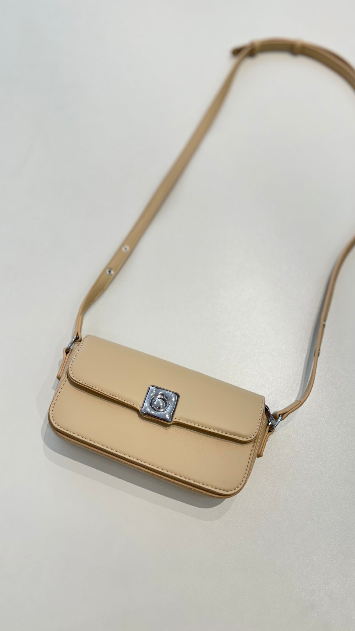 Bolsa Lia em couro legítimo bege, compacta e elegante. Design estruturado, alça regulável e detalhes em prata para usar no ombro ou transversal.
